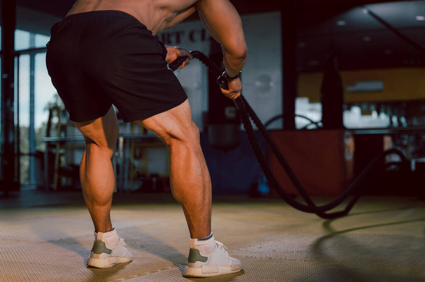 筋肉ボディービルダー フィットネスジムでバトルロープ練習で強力な若い男のトレーニング. フィットネスエクササイズ 戦闘ロープ装置と筋肉やボディービルを構築. - 写真・画像