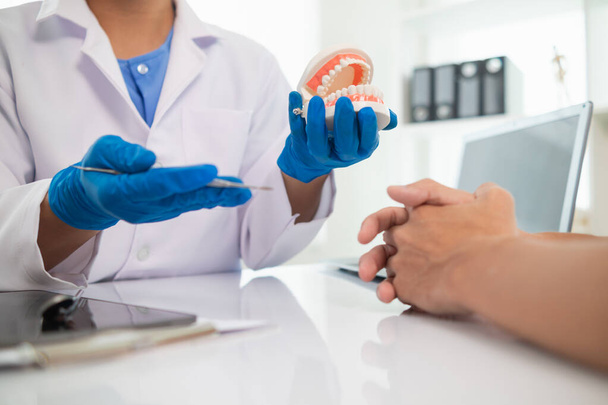 The dentist holds a denture in his hand and shows the patient the position of the problem tooth and the dentist explains how to treat the tooth for the patient to understand. Copy space for text - Photo, Image