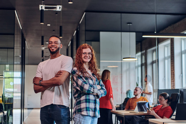 A young African American businessman and a modern businesswoman with orange hair stand side by side, arms crossed, exuding confidence and unity in a contemporary office setting, epitomizing dynamic - 写真・画像