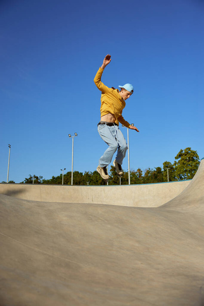 Skilled teenager boy wearing casual clothing and in roller blades jumping on ramp. Inline skates sport - Foto, Bild