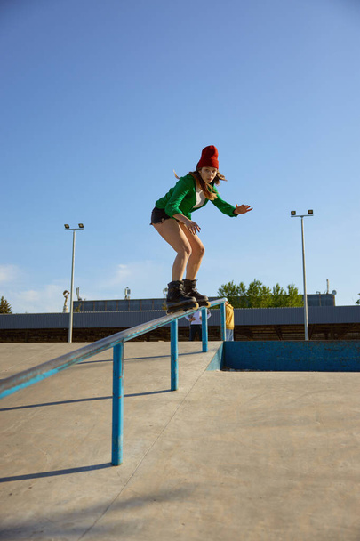 Talented teenager girl riding on handrail practicing extreme tricks. Dangerous roller skating stunt - Foto, Imagem