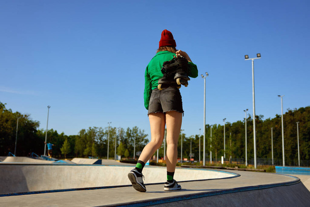 Casual κορίτσι μεταφέρουν rollerblades στα χέρια με τα πόδια στην τάξη κατάρτισης. Εξωτερική rollerdrome για εξάσκηση ταχύτητας freestyle ιππασίας - Φωτογραφία, εικόνα