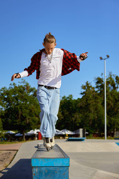 Teenager rollerskater balancing on pedestal performing extremely ride tricks. Recreation activity at skating park at summer day - Photo, image