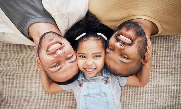 Portrait, gay dad and blended family with a girl lying together on the floor of the home for adoption from above. LGBT love, children or kids and a daughter with her happy foster parents in the house. - Photo, Image