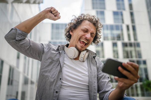 Yksi valkoihoinen mies istua ulkona ottaa jarru onnellinen hymy pelata videopelejä vapaa-ajan toimintaa hauskaa pidä matkapuhelimen käyttö älypuhelin hauskaa verkossa kopioi tilaa aikuinen mies - Valokuva, kuva
