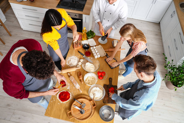 Gruppo di giovani con chef italiano che preparano la pizza durante il corso di cucina, vista dall'alto - Foto, immagini