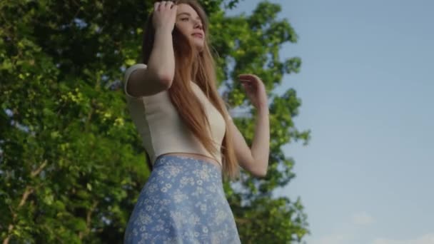 Vörös hajú, gyönyörű fiatal nő, zöld nyári parkban áll, pózol. Siker, szabadság és boldogság koncepció - Felvétel, videó