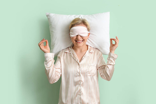 緑の背景で瞑想する枕を持つパジャマの若い女性 - 写真・画像