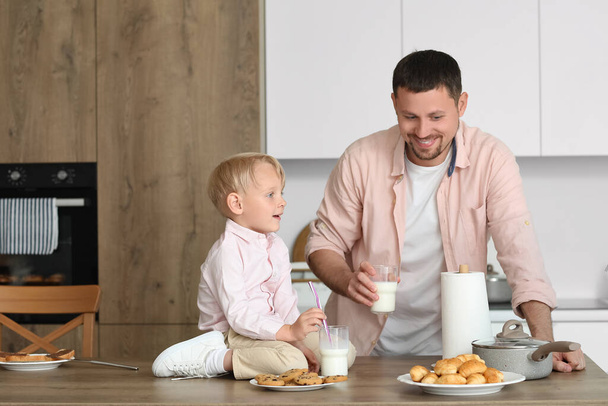 Mały chłopiec i jego ojciec z różnymi ciastkami pijący mleko w kuchni - Zdjęcie, obraz