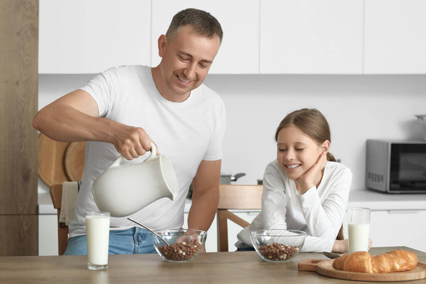 Niña con su padre comiendo bolas de maíz y bebiendo leche en la mesa de la cocina - Foto, imagen