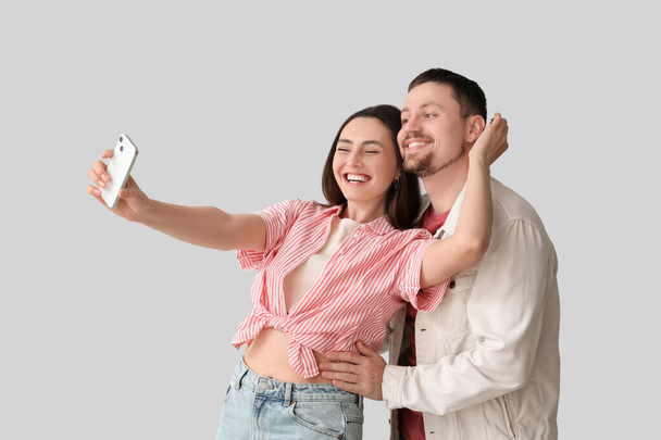 Feliz pareja joven con teléfono móvil tomando selfie sobre fondo claro - Foto, Imagen