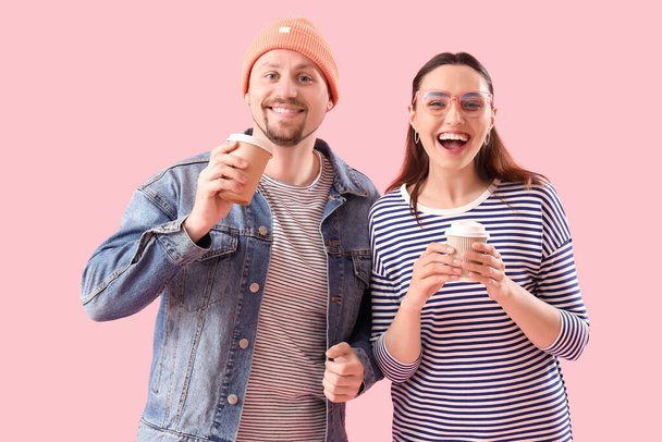 ピンクの背景にコーヒーのカップと幸せな若いカップル - 写真・画像