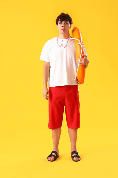 Man badmeester met ring boei fluitend op gele achtergrond - Foto, afbeelding
