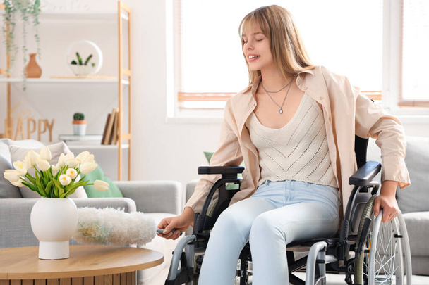 Młoda kobieta na wózku inwalidzkim sprzątanie tabeli z pp-duster w domu - Zdjęcie, obraz