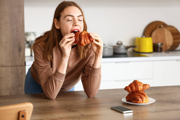 Bella giovane donna mangiare gustoso croissant in cucina - Foto, immagini