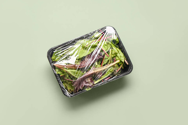 Hojas frescas de ensalada cubiertas con plástico para alimentos sobre fondo verde - Foto, Imagen
