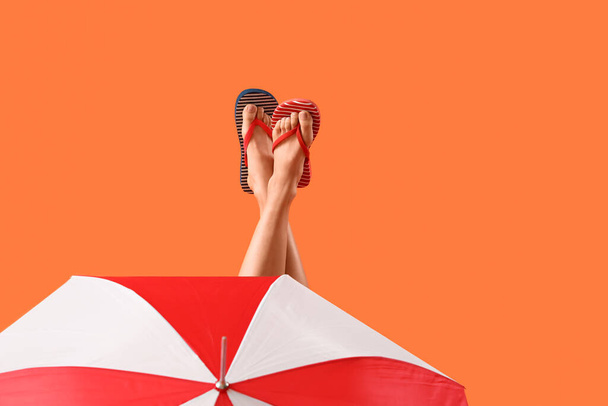 Зонтик и ноги молодой женщины в шлепанцах на оранжевом фоне - Фото, изображение