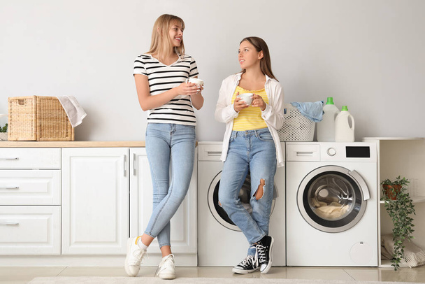 Studentinnen mit Kaffeebechern beim Wäschewaschen im Wohnheim - Foto, Bild