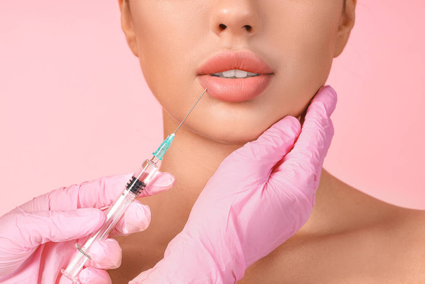 Jeune femme recevant une injection de lèvre sur fond rose, gros plan - Photo, image