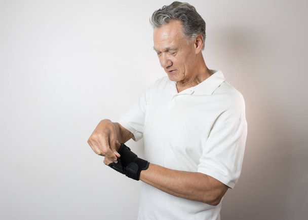 Homem Sênior usando uma cinta de pulso em sua mão esquerda e pulso para o controle da dor - Foto, Imagem
