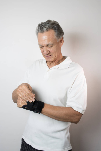 Homem Sênior usando uma cinta de pulso em sua mão esquerda e pulso para o controle da dor - Foto, Imagem