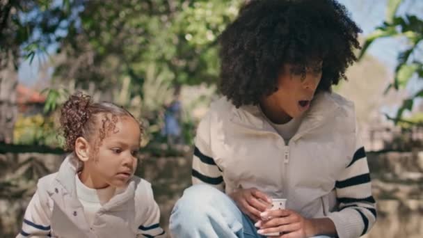 African american family exploring nature in beautiful green park closeup. Emotional young mother looking on something gesturing in talk. Cute little child listening mom enjoying sunny weekend together - Footage, Video