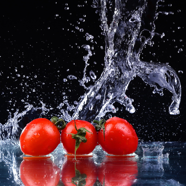 Studio shot with freeze motion of cherry tomatoes in water splash on black background - Photo, Image