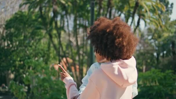 Nyugodt nő, gyereket vár, aki a Green Parkban sétál. Gondtalan afro-amerikai anya kezében kislánya sétál a napsütéses természet. Vonzó göndör anya élvezni gyönyörű növényzet szabadban. - Felvétel, videó