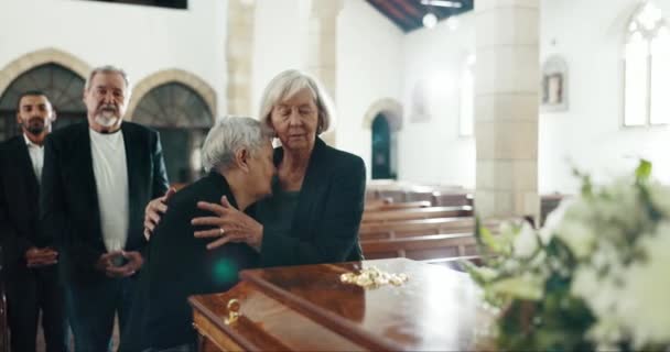 Starsze kobiety, przytulić i pogrzeb w kościele dla wygody, wsparcia i opieki z płaczem, smutku i religii. Rodzina, przyjaciele i uścisk śmierci, straty i pocieszenia z miłości, empatii i wiary przez trumnę. - Materiał filmowy, wideo
