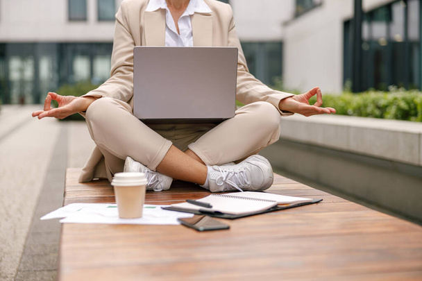 Directora mujer enfocada sentada en posición de loto y meditación durante el descanso con el trabajo en línea - Foto, imagen