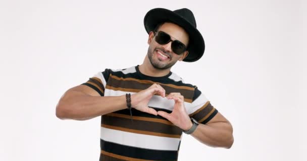 Fashion, hands in heart and man on a white background with trendy clothes, style and sunglasses. Happy, relax and portrait of isolated person with hand gesture, symbol and emoji for love in studio. - Footage, Video