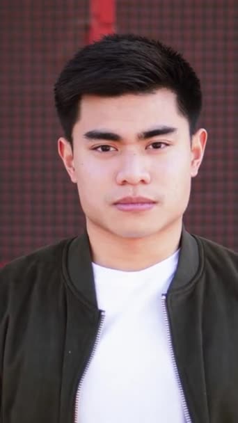 Vertical individual close Up Portrait of Serious asian guy Looking at Camera standing outdoors. Young adult man staring front outside with pernsive expression. High quality footage - Footage, Video