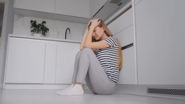 Молодая женщина, страдающая депрессией, сидит на полу в кухонной комнате. Проблемы психического здоровья. - Кадры, видео