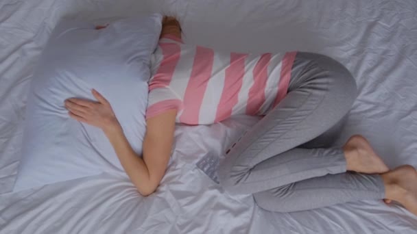A young woman suffers from menstrual pain. Woman clutching her stomach with her hands and having painful stomach pain or menstrual cramps while lying on the sofa, stomach ache concept. - Footage, Video