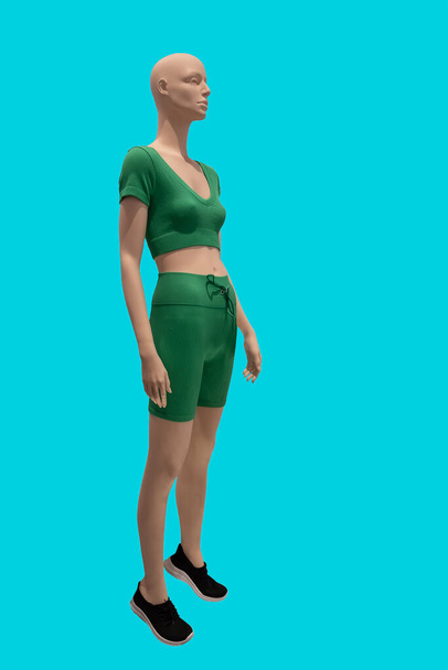 Immagine a figura intera di un manichino femminile che indossa abbigliamento sportivo stretto con top in maglia verde e pantaloncini isolati su sfondo blu - Foto, immagini