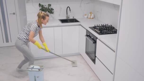 Het werk van een schoonmaakbedrijf. Een vrouwelijke werkster maakt het huis schoon. Natte reiniging met een dweil. - Video