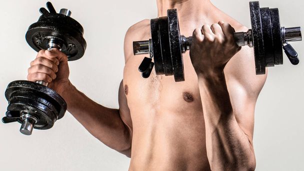 Weak man lift a weight, dumbbells, biceps, muscle, fitness. Man holding dumbbell in hand. Skinny guy hold dumbbells up in hands. Thin man in sports with dumbbells. - Photo, Image