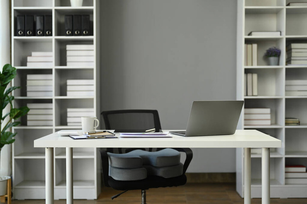 Moderno ufficio interno con computer portatile, documenti e tazza di caffè su tavolo bianco contro parete grigia.. - Foto, immagini