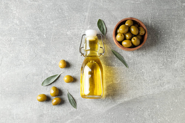 Бутылка оливкового масла и оливок в миске на сером фоне, вид сверху - Фото, изображение