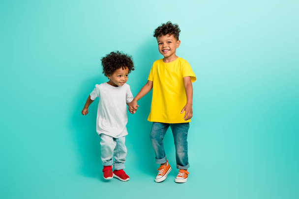Full size photo of two adorable small boys friendly brothers hold hands have fun wear trendy outfit isolated on aquamarine color background. - Photo, Image