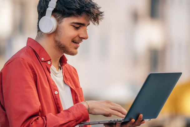 young male with headphones and laptop in the street - Photo, Image