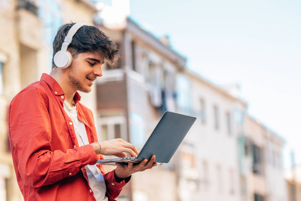 young man with laptop and headphones outdoors in the city - Photo, Image