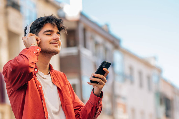 молодий чоловік зі смартфоном або мобільним телефоном та навушниками на відкритому повітрі у місті - Фото, зображення