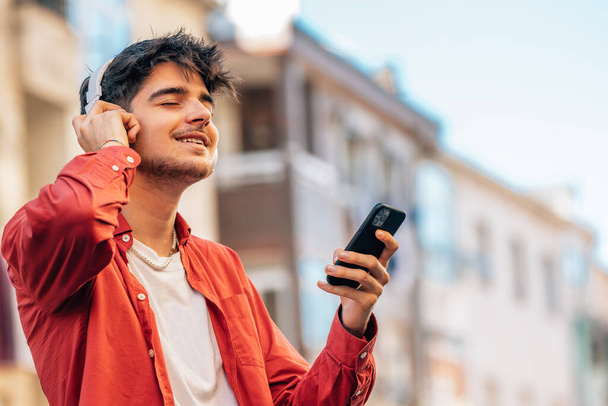 молодий чоловік зі смартфоном або мобільним телефоном та навушниками на відкритому повітрі у місті - Фото, зображення