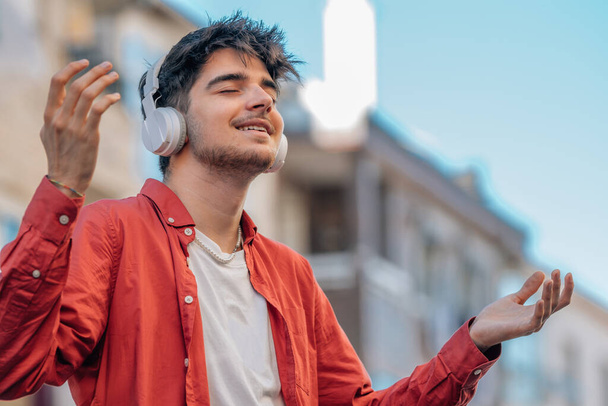 Молодой человек с наушниками расслабился, наслаждаясь музыкой на открытом воздухе - Фото, изображение