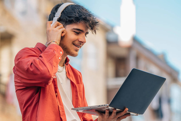 young man on the street with headphones and laptop outdoors - Photo, Image