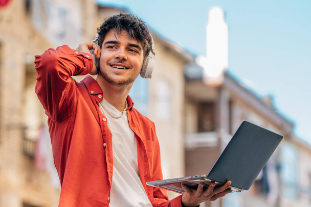 молодой человек на улице с наушниками и ноутбуком на открытом воздухе - Фото, изображение