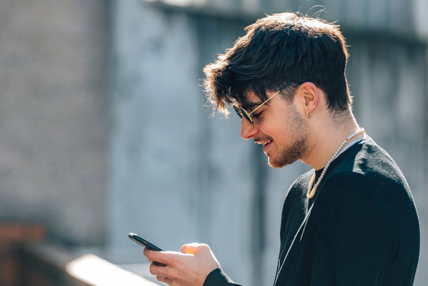 portrait of young man with sunglasses in the street with mobile or cell phone - Photo, Image