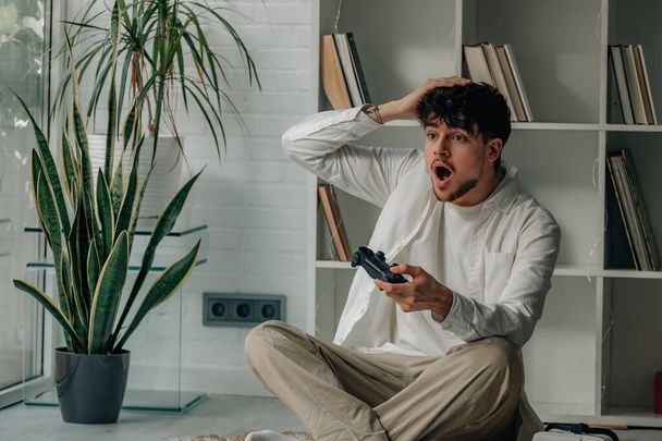 νεαρός άνδρας στο σπίτι με joystick παίζει βιντεοπαιχνίδι - Φωτογραφία, εικόνα