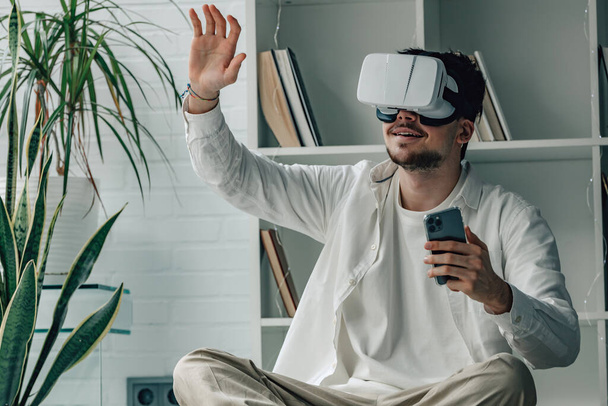 jonge man thuis met virtual reality bril en mobiele telefoon - Foto, afbeelding